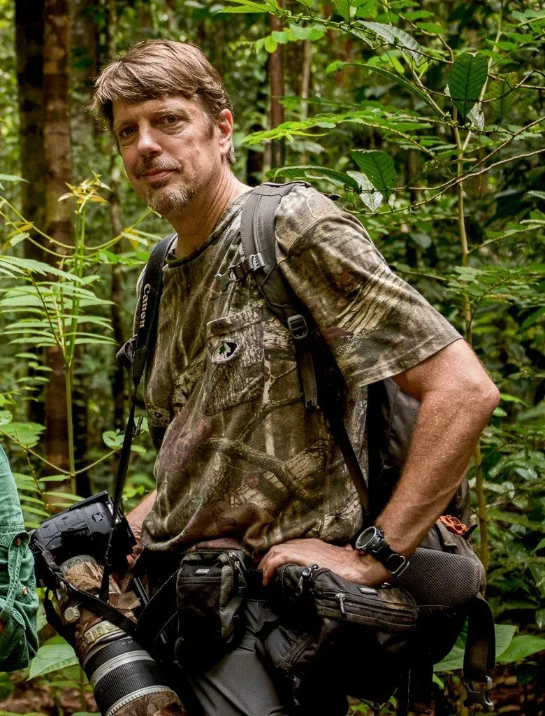 Tim Laman in camouflage gear with a telephoto lens in the field